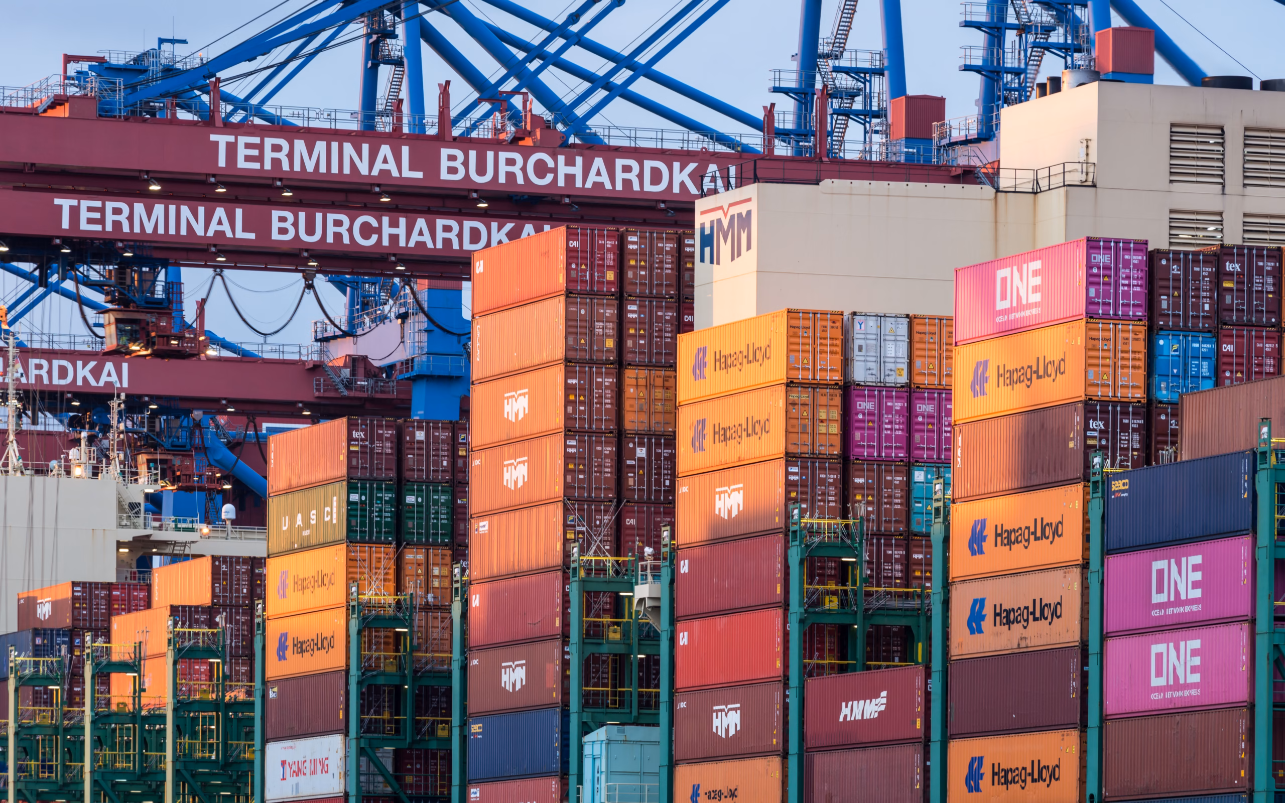 Container stacks from multiple shipping lines (HMM, ONE, Hapag-Lloyd, Yang Ming) at Terminal Burchardkai Hamburg — illustrates outdoor gear wholesale container consolidation strategy