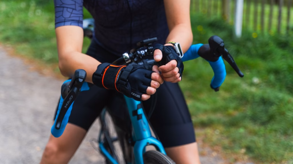 A close-up view of a cyclist wearing black and red fingerless cycling gloves gripping the handlebars.